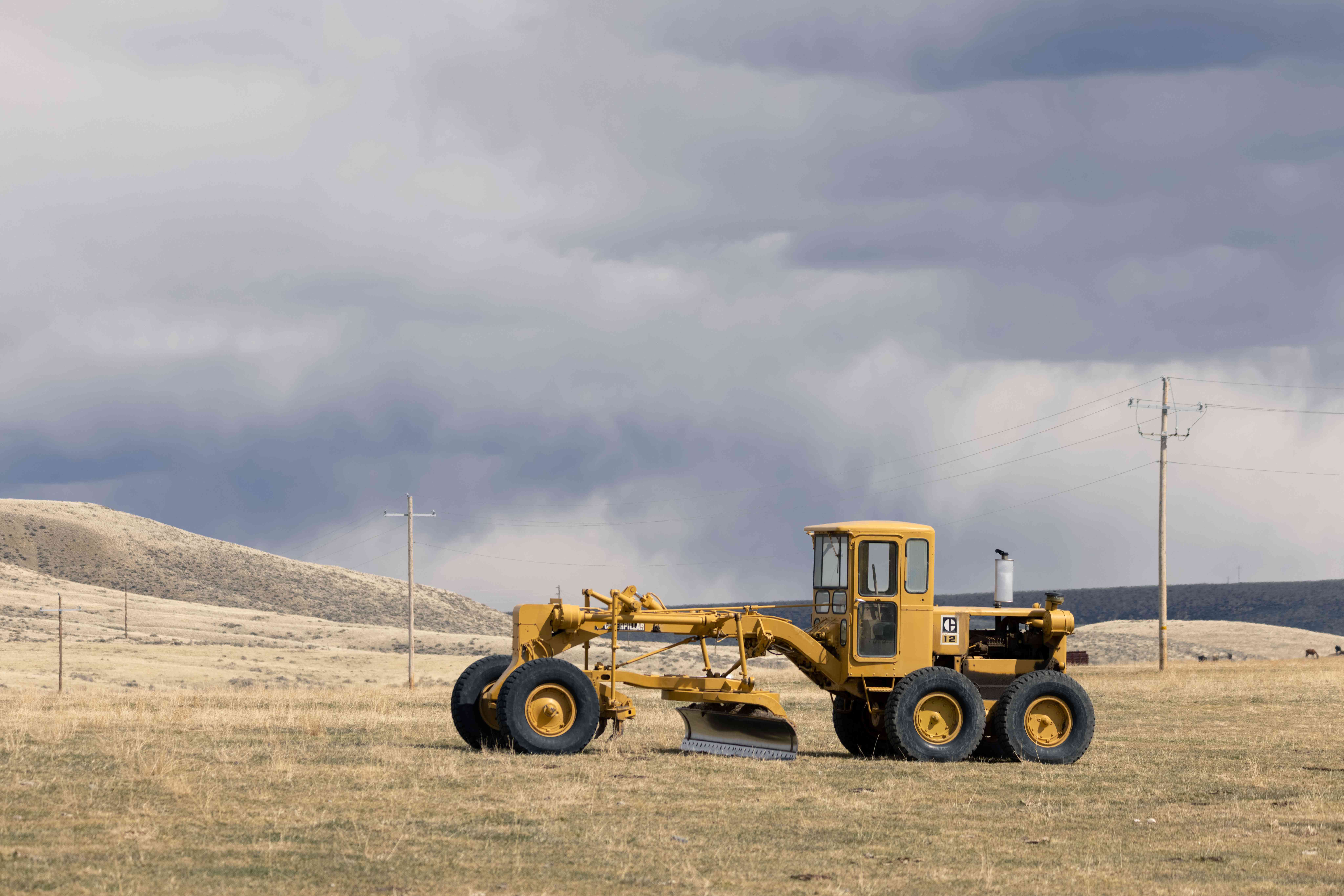 大型黄色商用拖拉机在草原农场耕田，天空阴沉