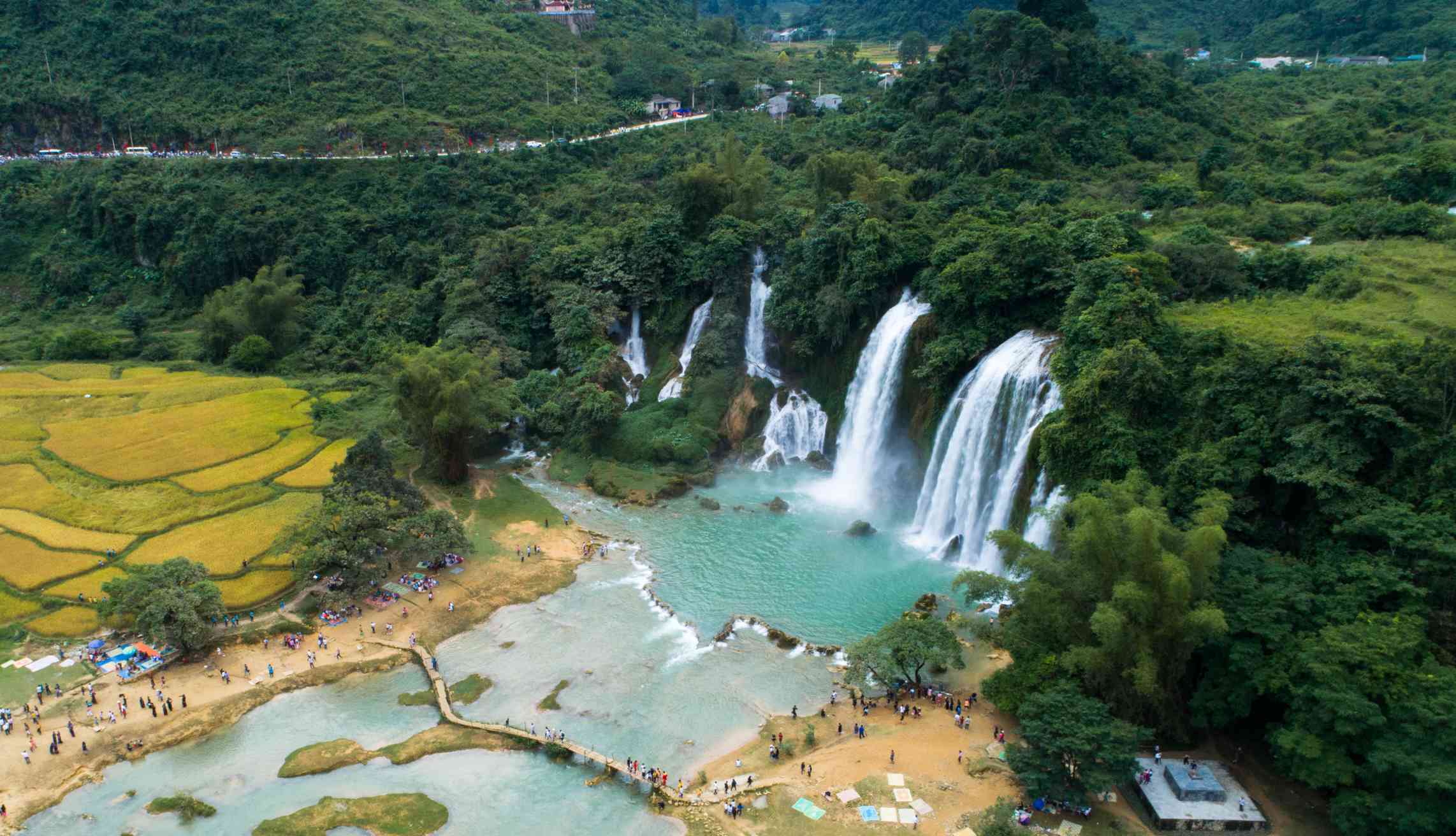 Ban Gioc-Detian瀑布的鸟瞰图，许多瀑布从郁郁葱葱的绿色山峰流入一个充满清澈绿色水的池塘＂width=