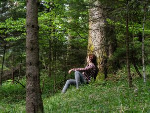 女人靠在树木茂密的森林中深处的树木上