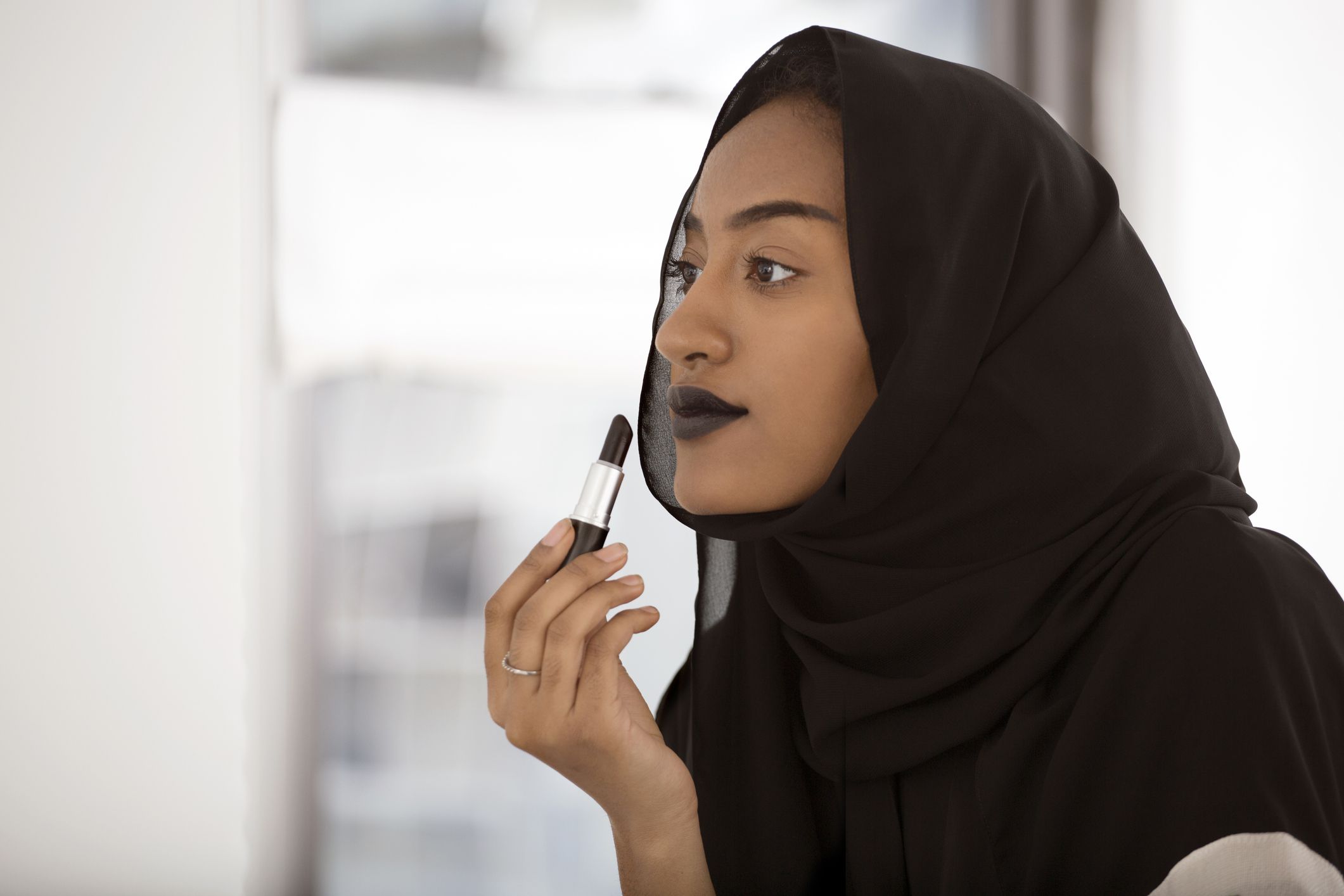 一位穆斯林妇女在镜子前涂深色口红。