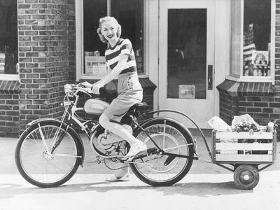 一个女人骑着一辆带货物拖车的自行车的复古照片。