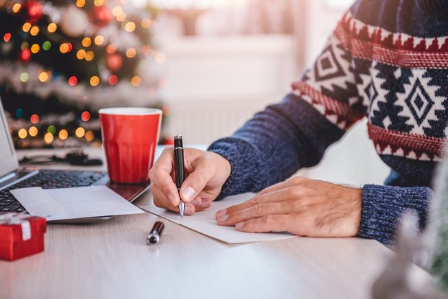 一个人在一件毛衣写圣诞贺卡在桌子附近的一棵圣诞树