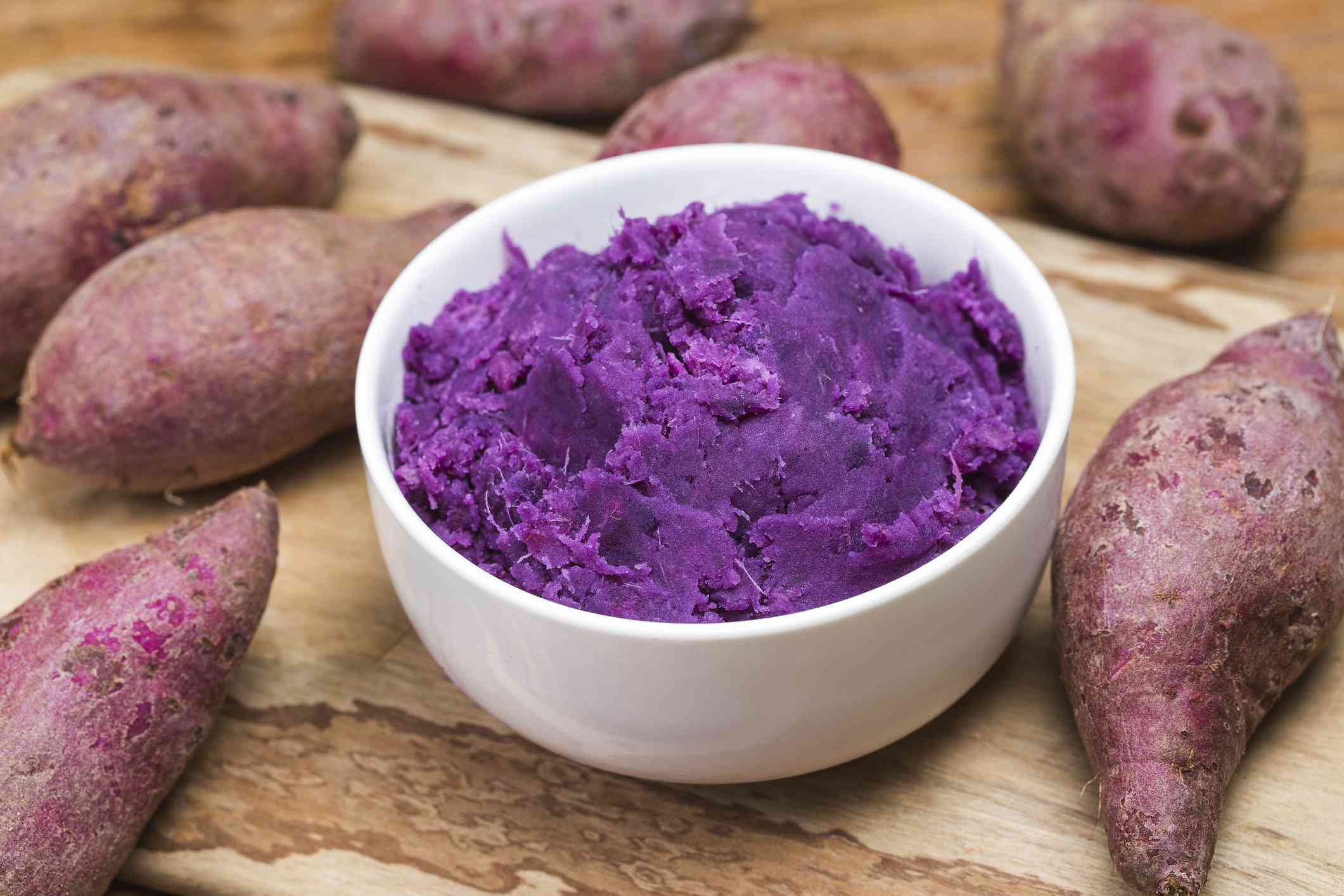 捣碎的紫色红薯放在白色的碗里，周围是生的