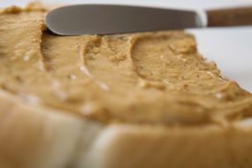 特写的刀子把花生酱均匀在一片面包上