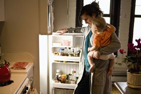 母亲抱着儿子在冰箱里找食材＂width=