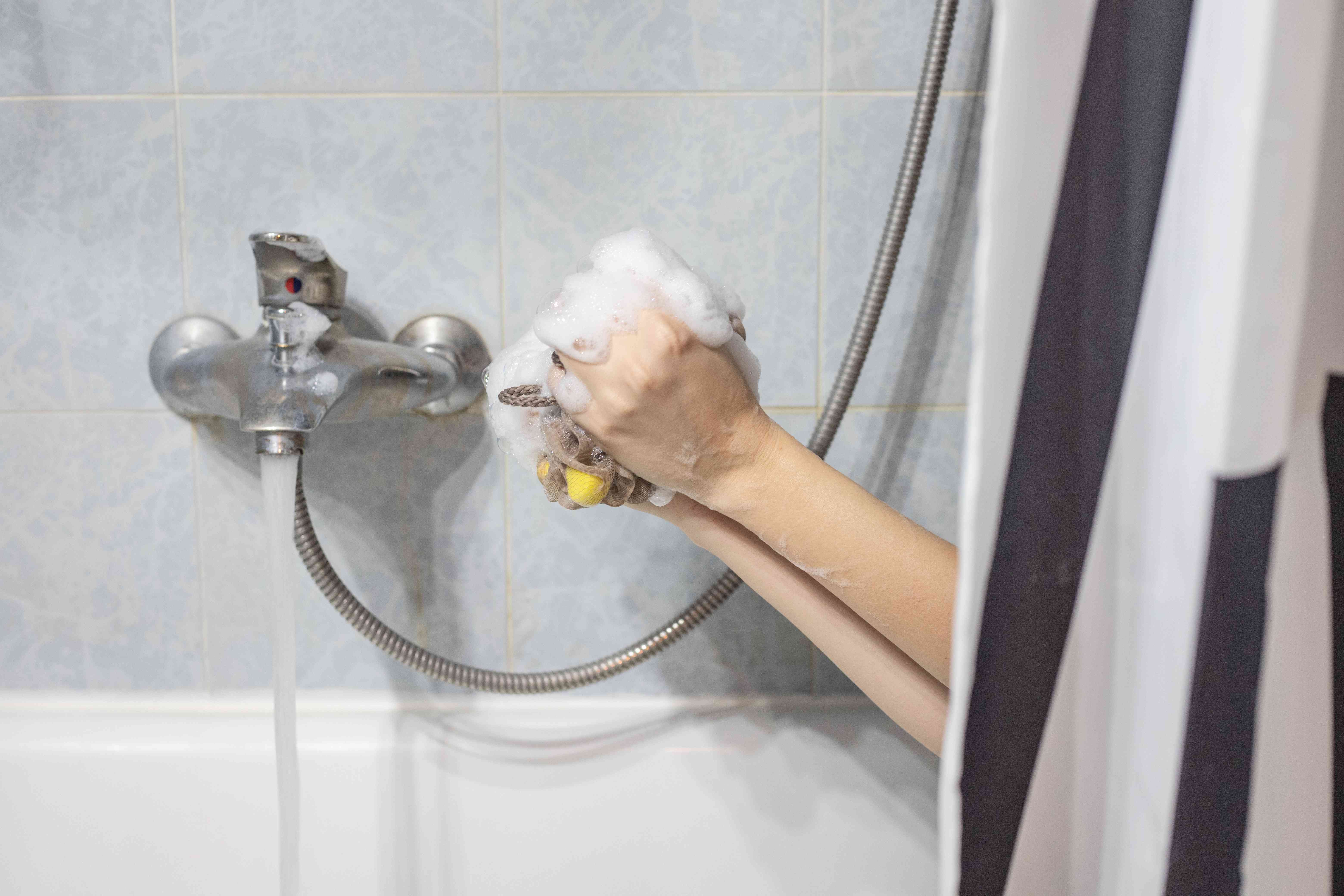 人把手从浴缸里探出来，用丝瓜络制造肥皂泡沫