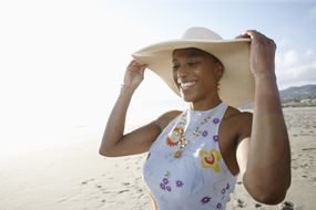 海滩上戴太阳帽的妇女＂width=