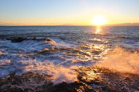 日落时的岩石海岸，光线在波浪中扩散＂width=