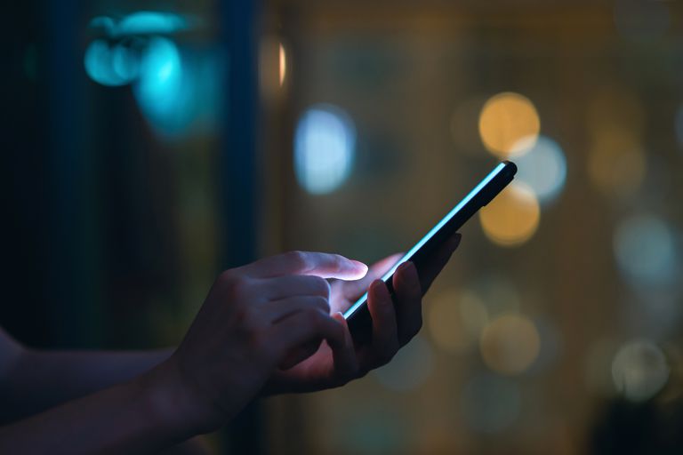 女性在黑暗中使用智能手机的手特写，在城市灯光的衬托下