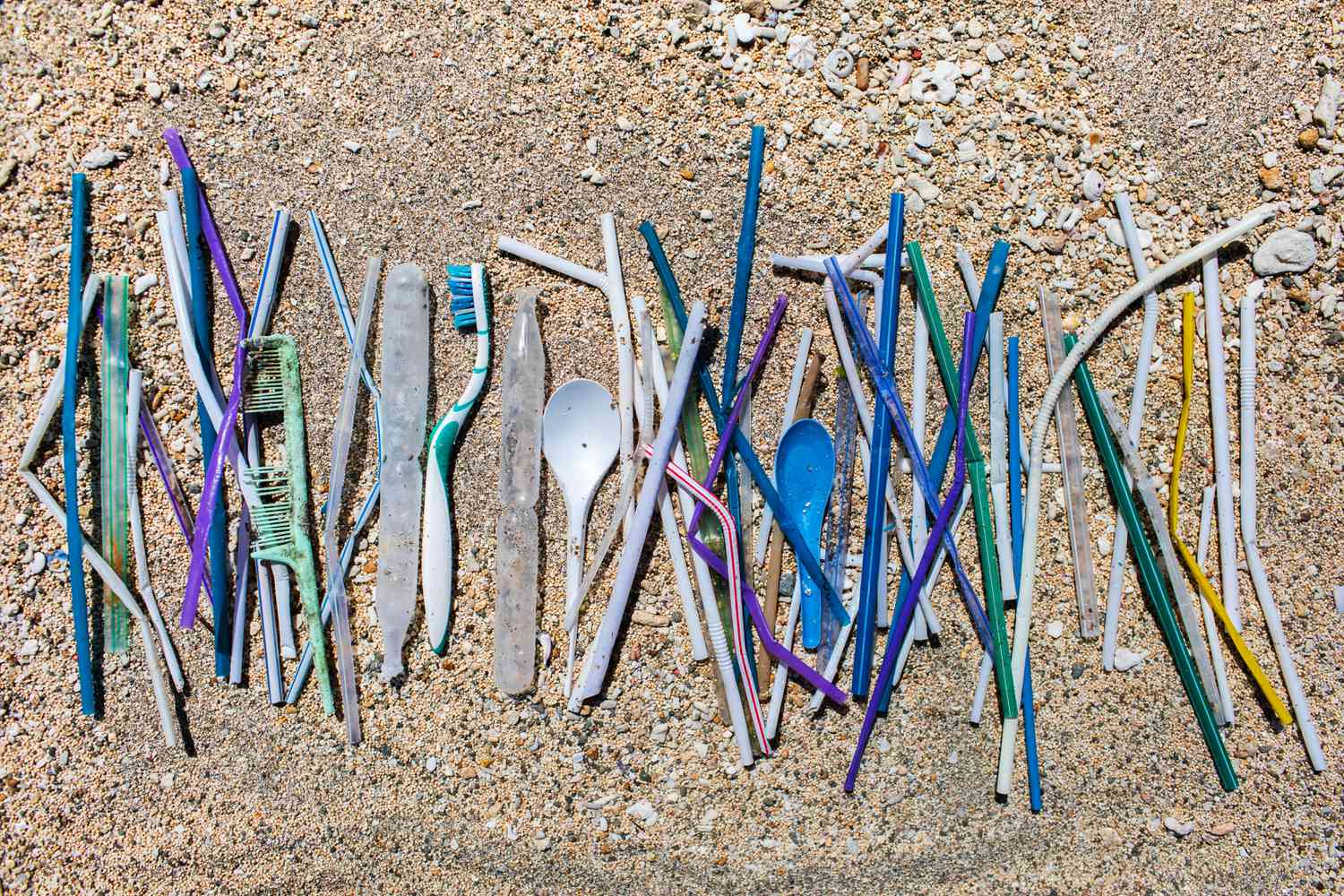 堆不同的塑料垃圾:吸管和一次性勺子,牙刷和梳子在海滩上收集在沙地上的背景