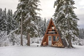 带有柴火的A型木屋坐落在白雪皑皑的森林中