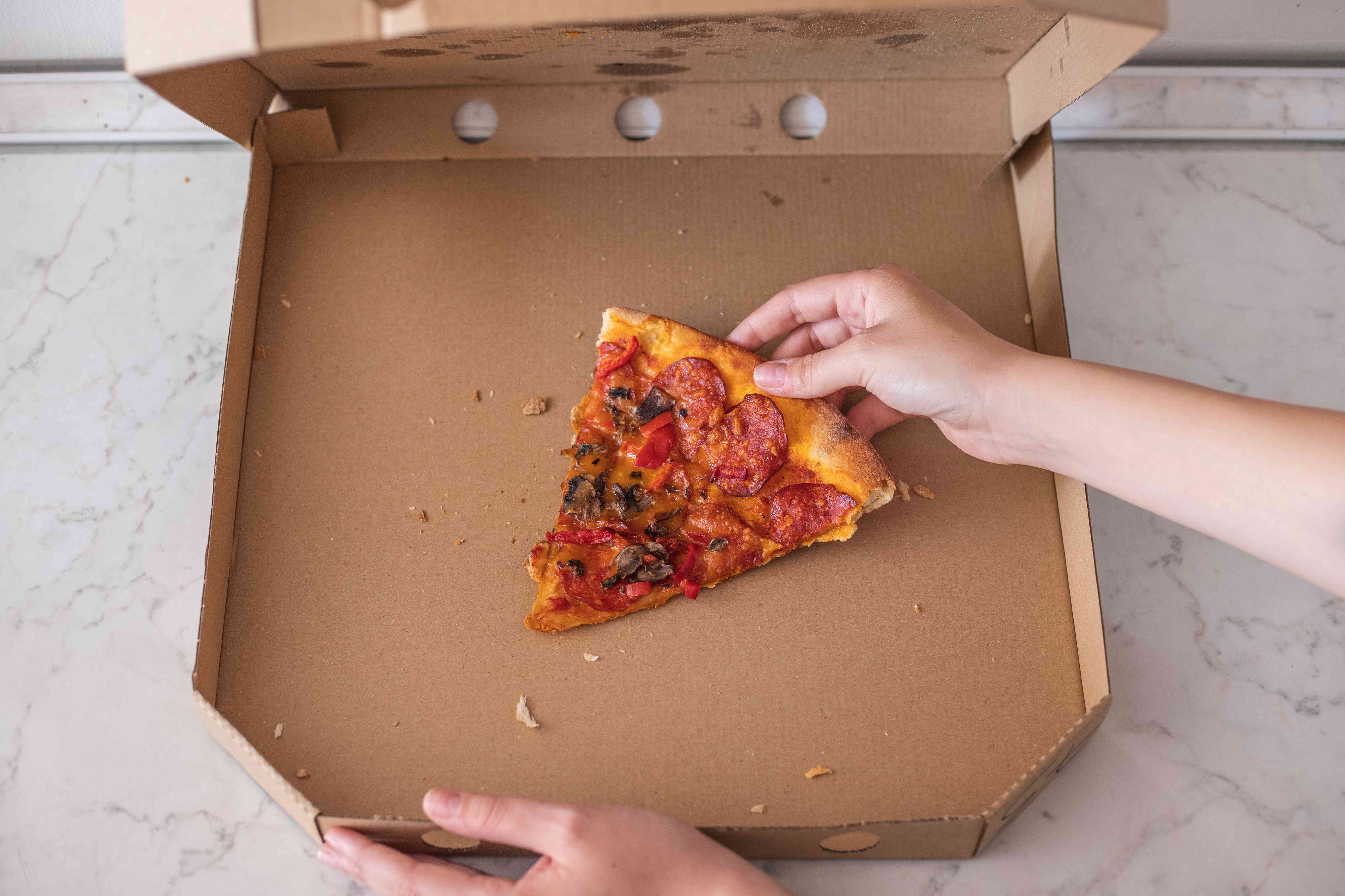 手伸向打开的披萨纸盒里的最后一片披萨