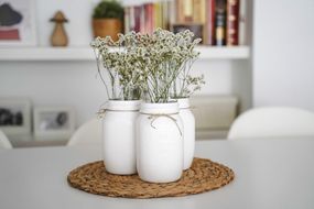 桌子上画着白色的玻璃瓶，上面放着花。＂width=