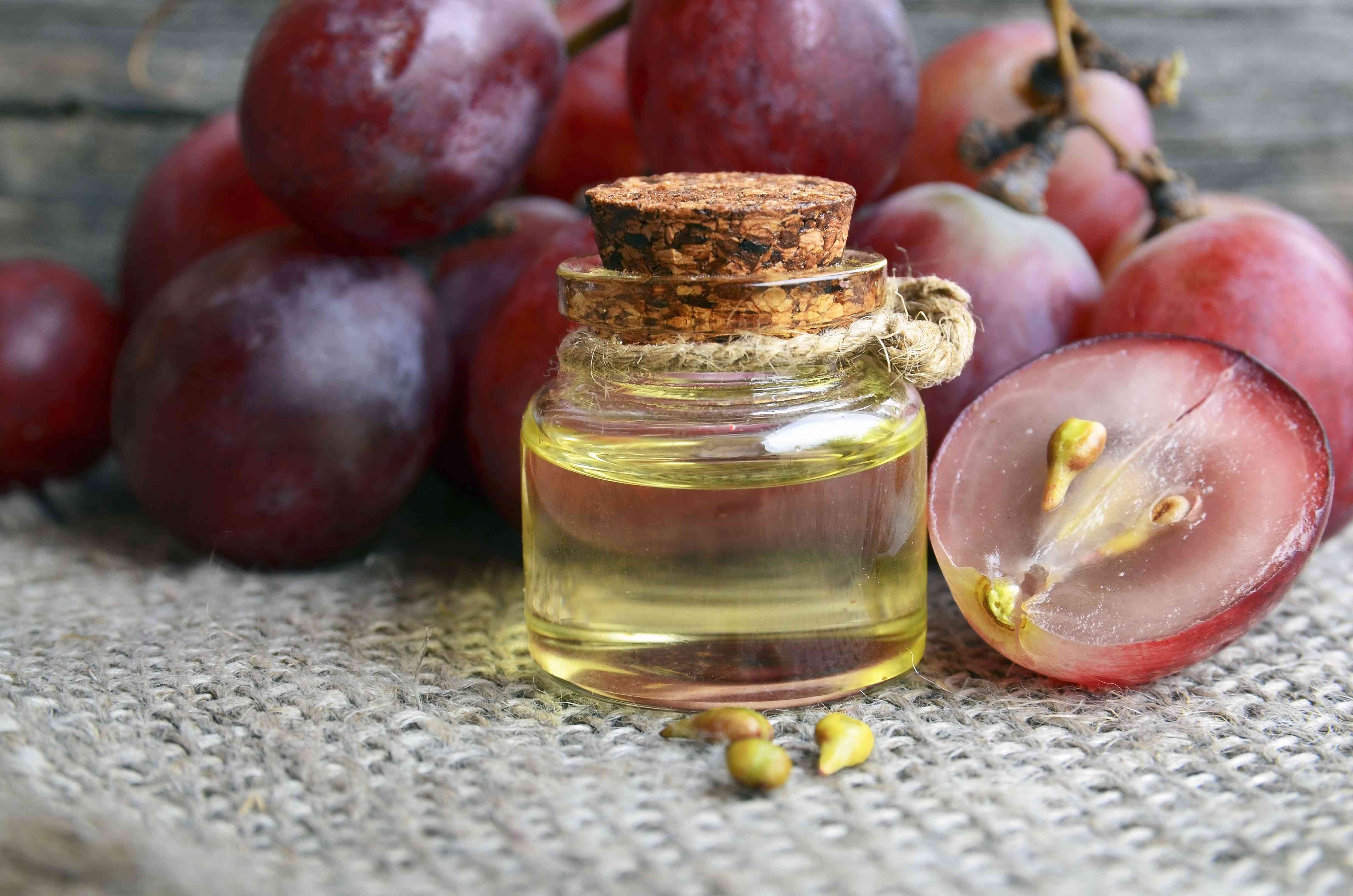 一瓶有机葡萄籽油温泉和身体护理和新鲜成熟的葡萄浆果在旧木桌。健康食品，生物，生态产品概念。