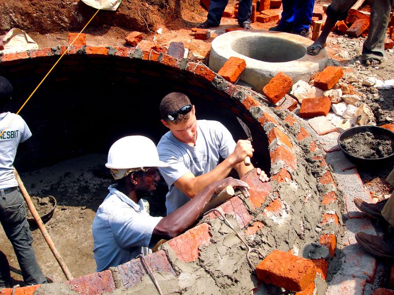 学员伊桑·德瓦特(Ethan Dewart)正在与一名乌干达建筑工人一起用砖块和灰泥建造一个沼气池圆顶