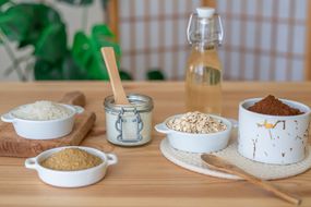 各种用于自然去角质的食物，包括燕麦，糖，盐，都放在桌子上的容器里＂width=