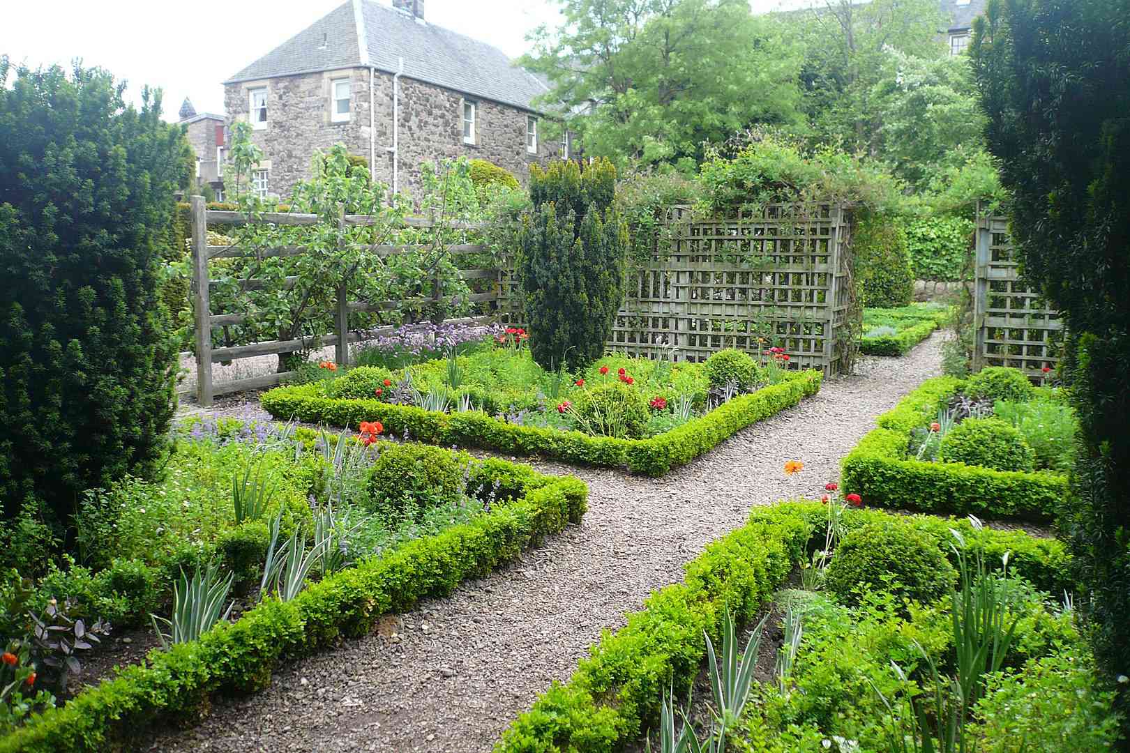 小径穿过Dunbar's Close Garden，这是一个有序的花园，小的，绿色的地面覆盖着植物床，里面种着较大的绿色植物和高大的灌木，有木棚架和远处的小教堂