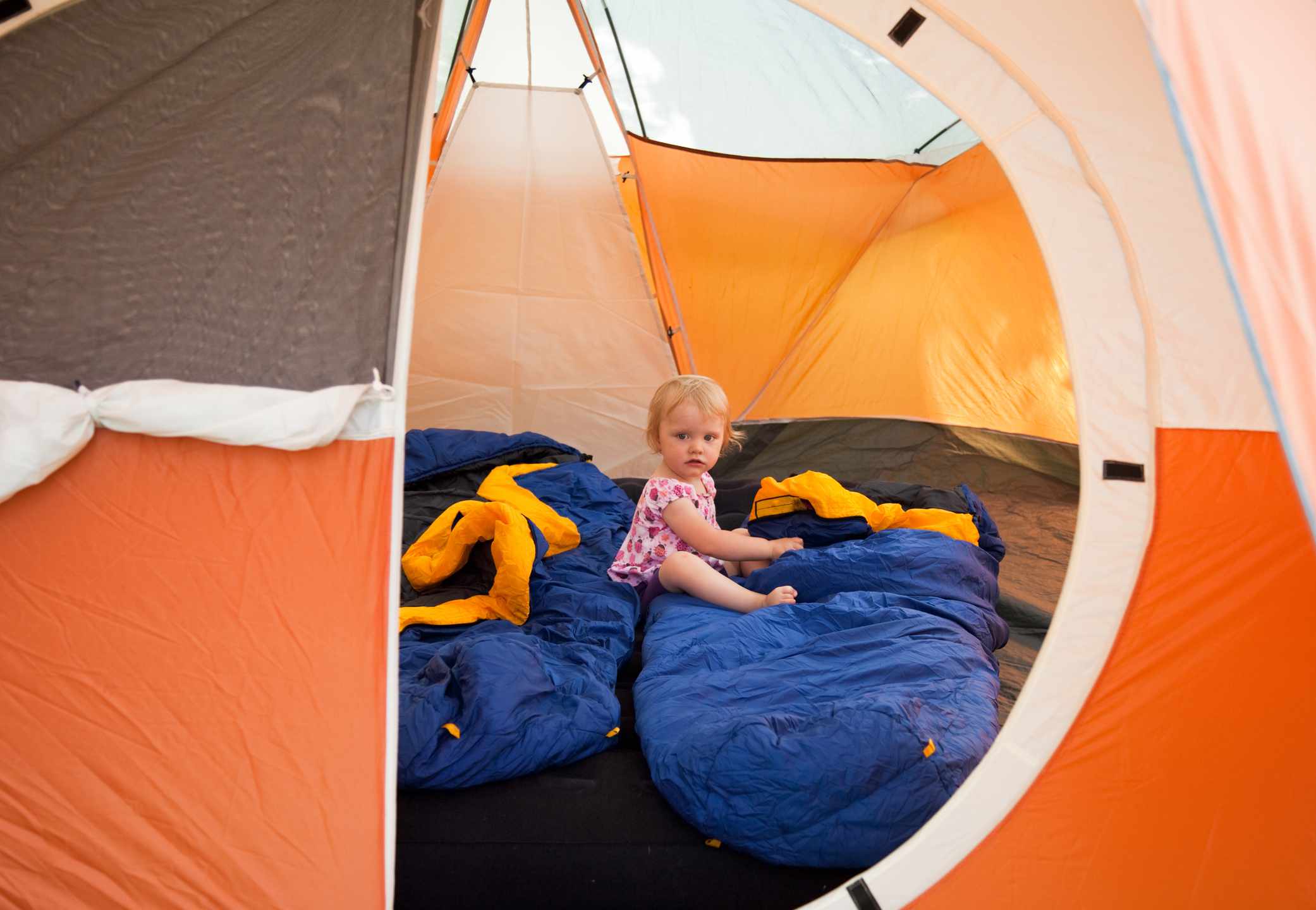小女孩坐在帐篷里的睡袋上。