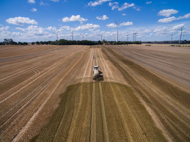 一辆卡车在德国的一个田野上散布肥料，风力涡轮机站在地平线上