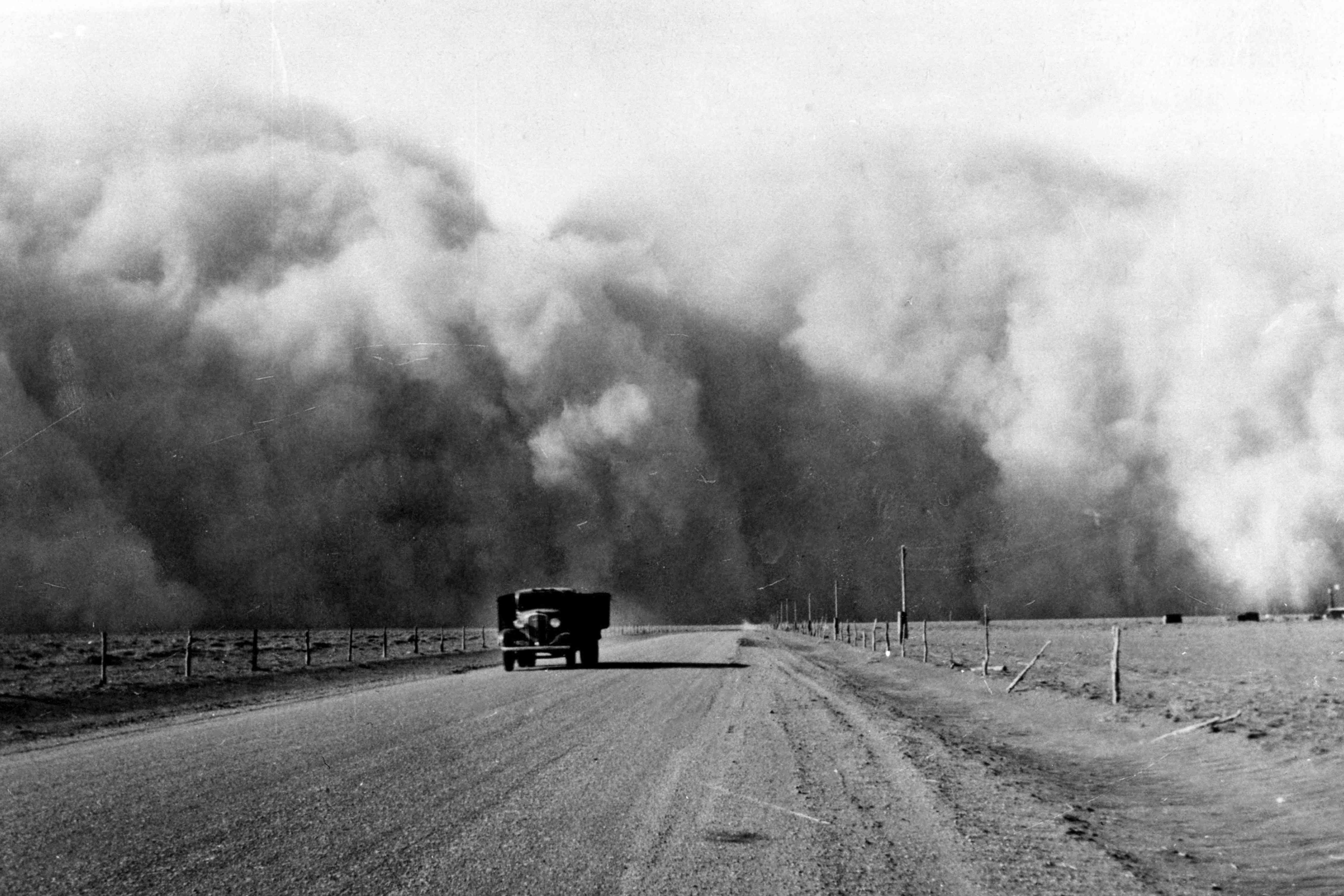 尘埃云填满了天空，卡车在远离土路的土路上驱动“width=