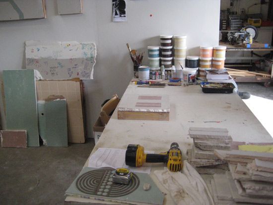 一个艺术家工作室，有一张装满颜料的桌子，一个钻头和瓷砖。