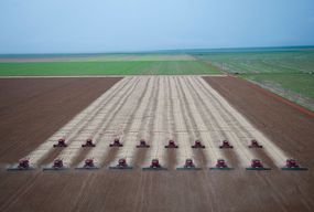 在巴西马托格罗索州的一个农场，成排的联合收割机正在收获大豆，周围是绿色的田地。