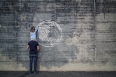 奥地利萨尔斯堡,父亲和女儿在自己的肩膀上,女儿用粉笔画地球在混凝土墙