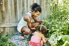 黑人母亲和女儿蹲在后院花园的木栅栏旁