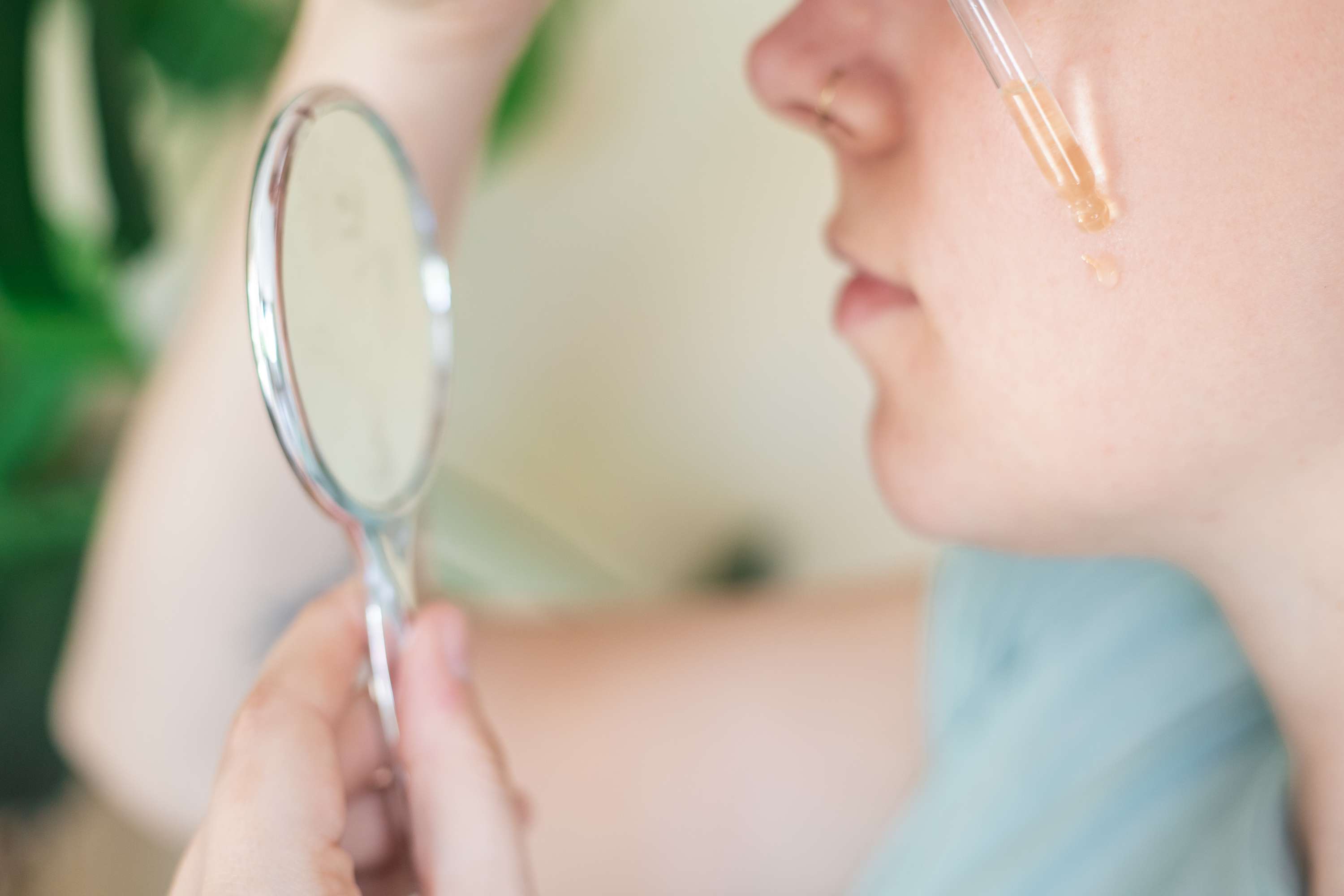 妇女用小镜子和玻璃滴管将辣木油涂抹在脸上的斑点上＂width=