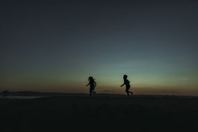 兄弟姐妹在黄昏奔向海洋的剪影＂width=