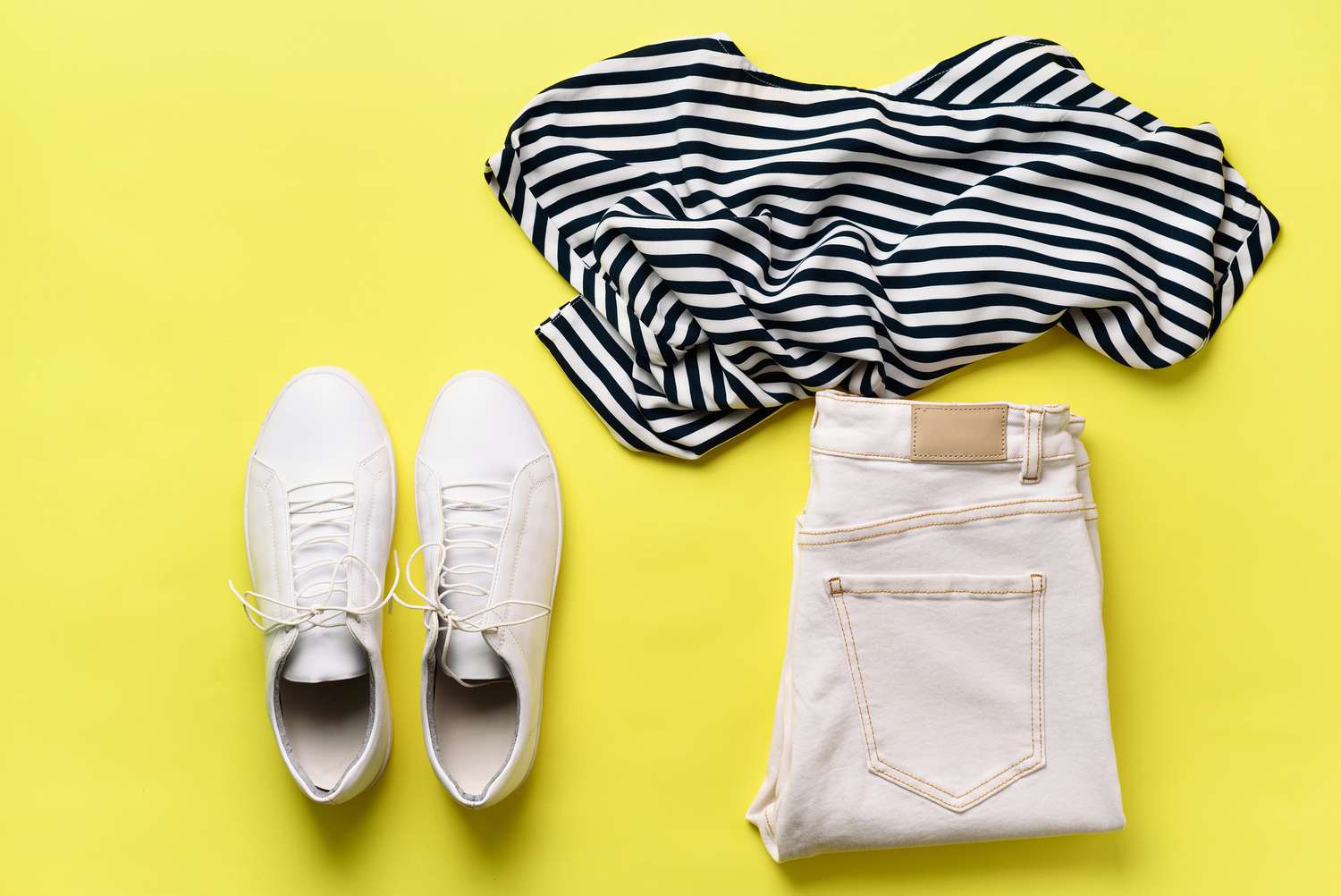 女性白色运动鞋和牛仔裤，条纹t恤在黄色背景与复制空间。前视图。夏季时尚，胶囊衣橱概念。创意平面躺