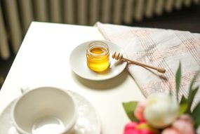 jar of honey with wooden dipper sits on table with flowers