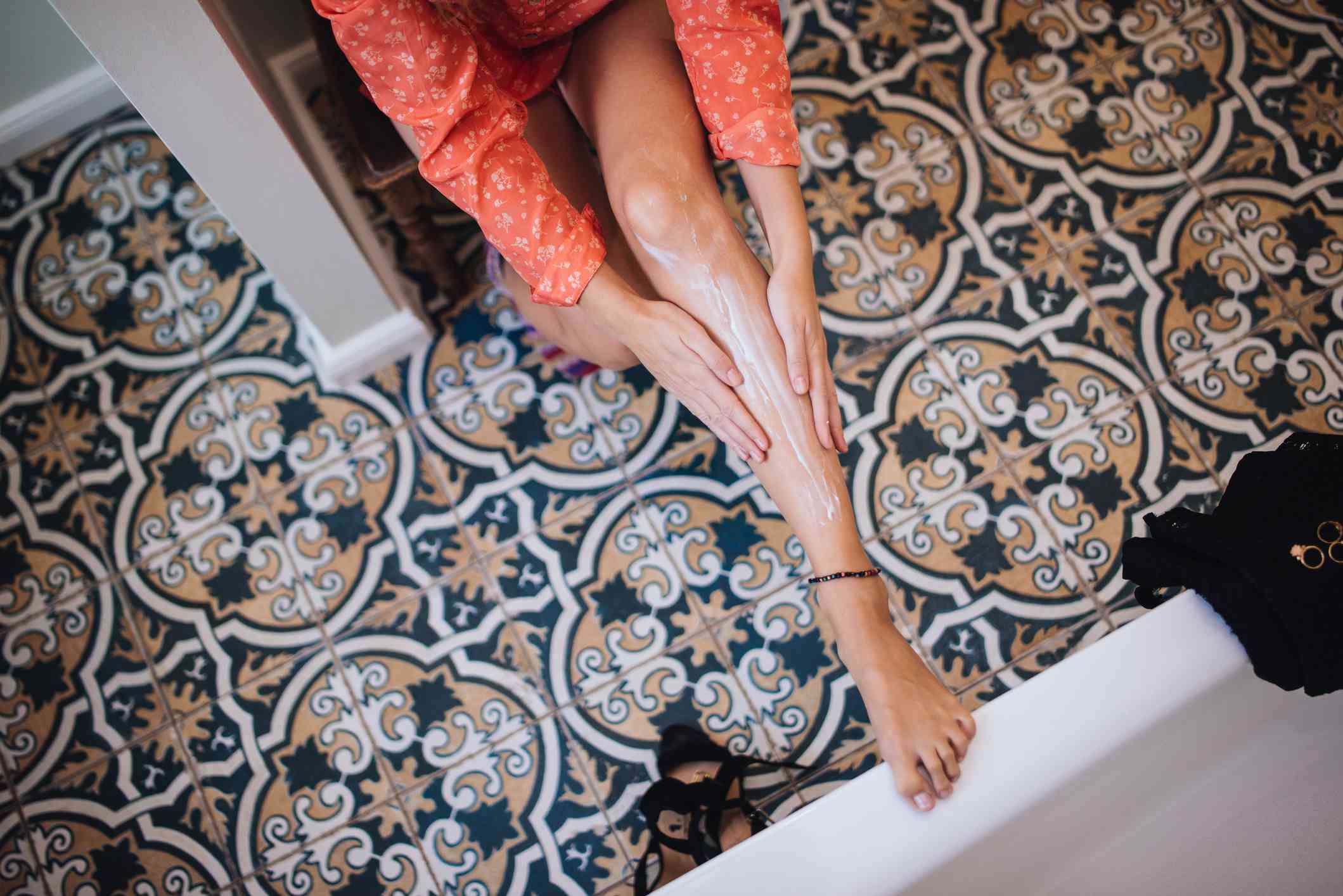 一名妇女在一间铺着复杂瓷砖的洗手间里往腿上涂乳液。