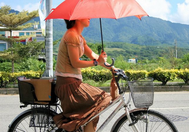 骑自行车的妇女，当佩带裙子和运载一把红色伞