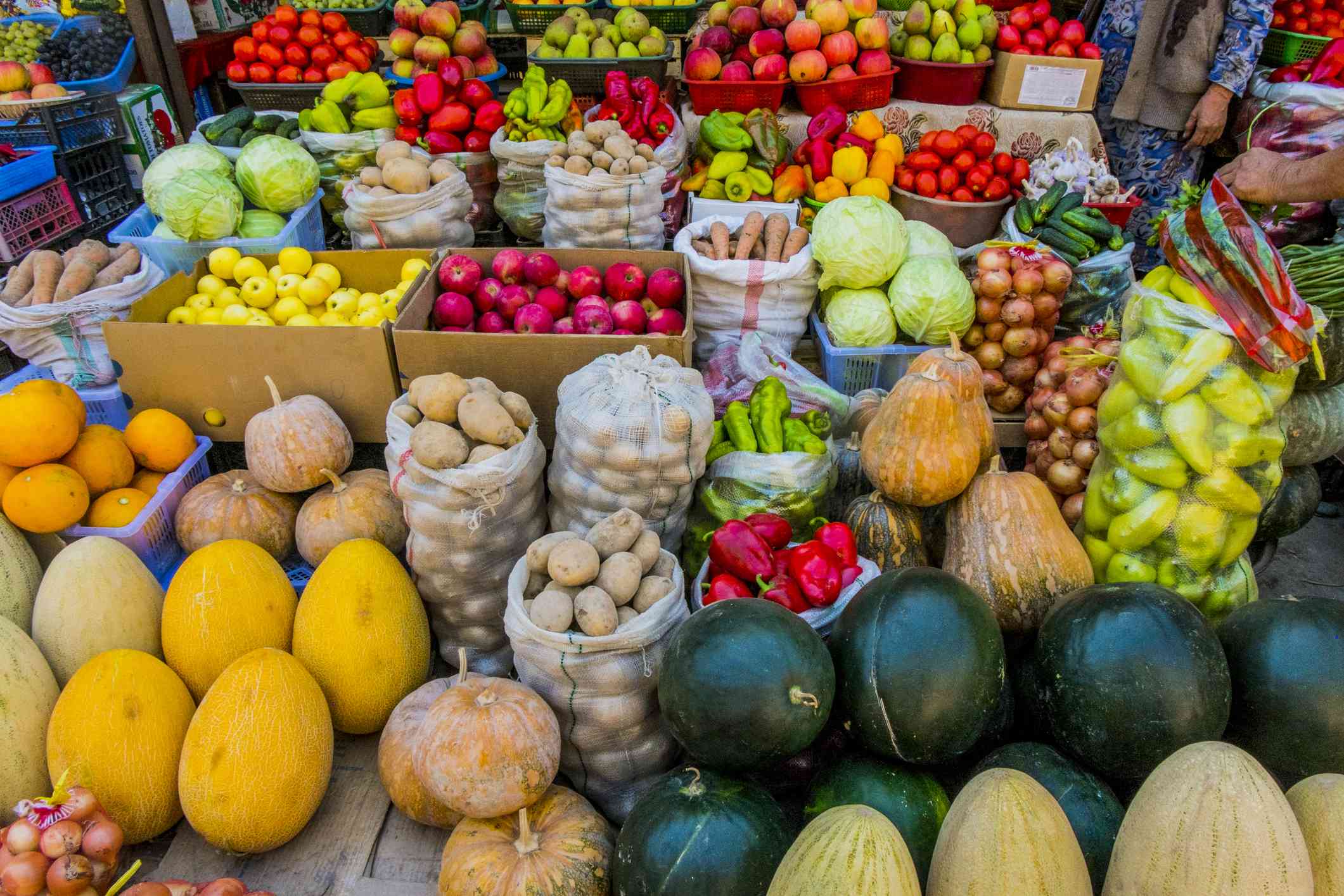 各种各样五颜六色的水果和蔬菜，包括瓜、南瓜、西红柿、土豆和苹果，在农贸市场的桌子上、盒子里和袋子里