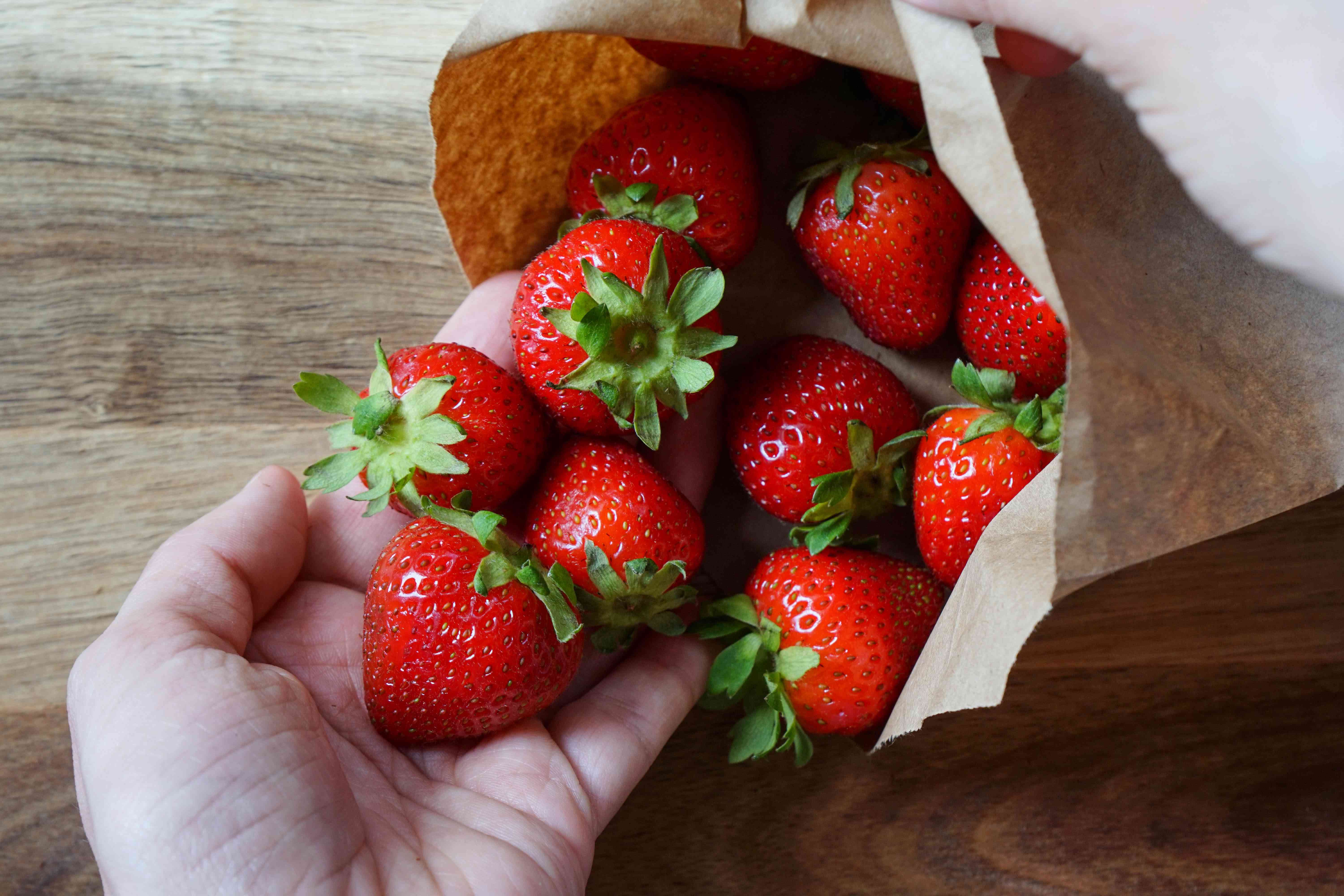 双手捧着新鲜的草莓，从棕色纸袋里溢出来