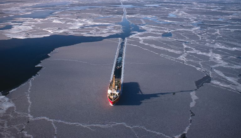 在一个阳光明媚的日子里，一艘船在北冰洋的海冰上开路。＂class=