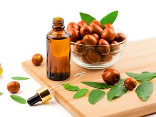 荷荷巴油装在瓶子里，用滴管滴在木桌上，木桌上放着成熟的荷荷巴果实。枣子油和水果