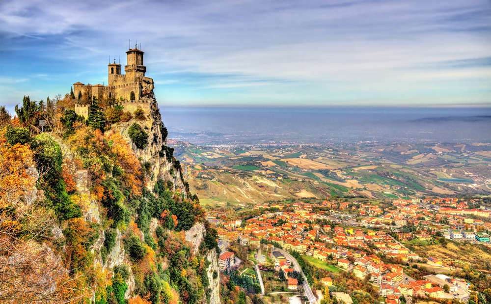圣马力诺的一座城堡坐落在悬崖上，俯瞰着下面广阔的山谷小镇