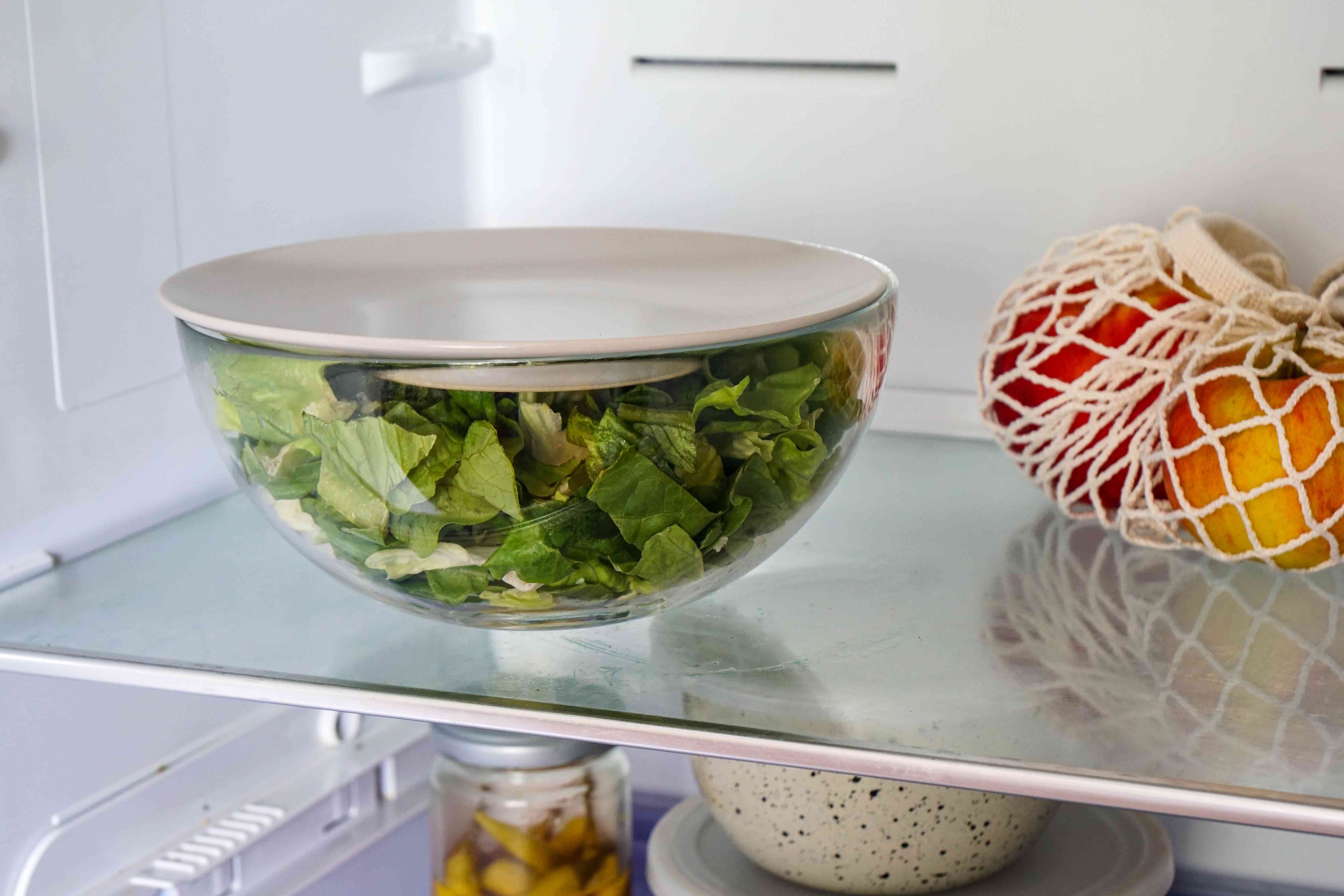 盛满生菜的玻璃碗，用盘子作为盖子储存在冰箱里
