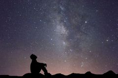 一个人的轮廓坐在地面上，抬头看着星空的天空