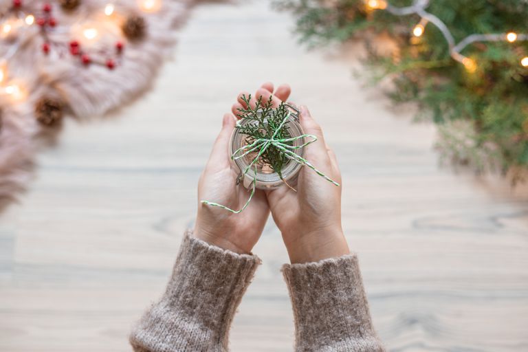 手伸出用麻绳和冷杉树枝包裹的玻璃罐作为环保圣诞包装礼物