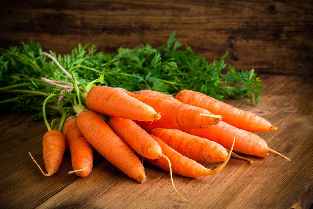 一串新鲜的胡萝卜和绿色蔬菜放在木桌上＂width=