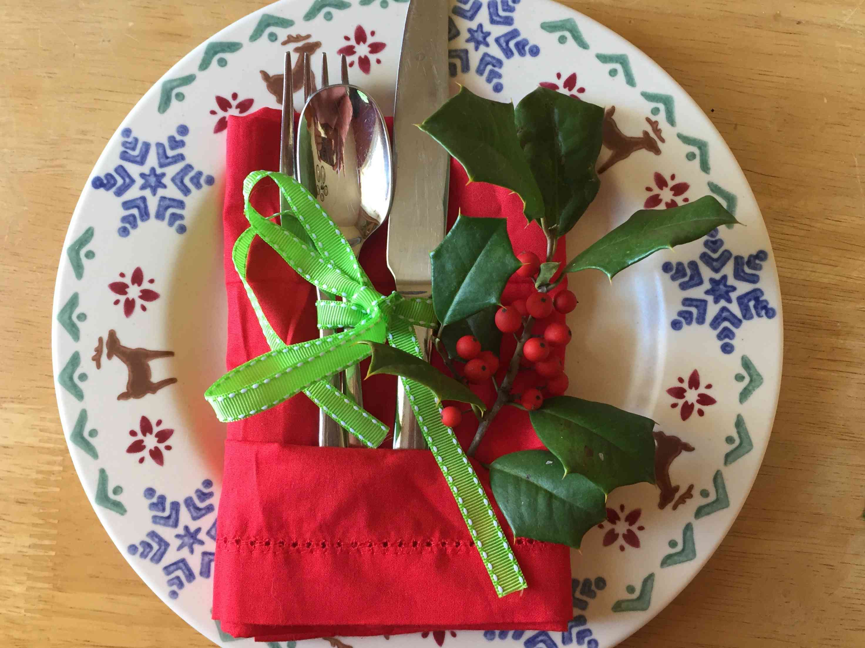 红布餐巾折叠成礼物形状，将银器固定在盘子上