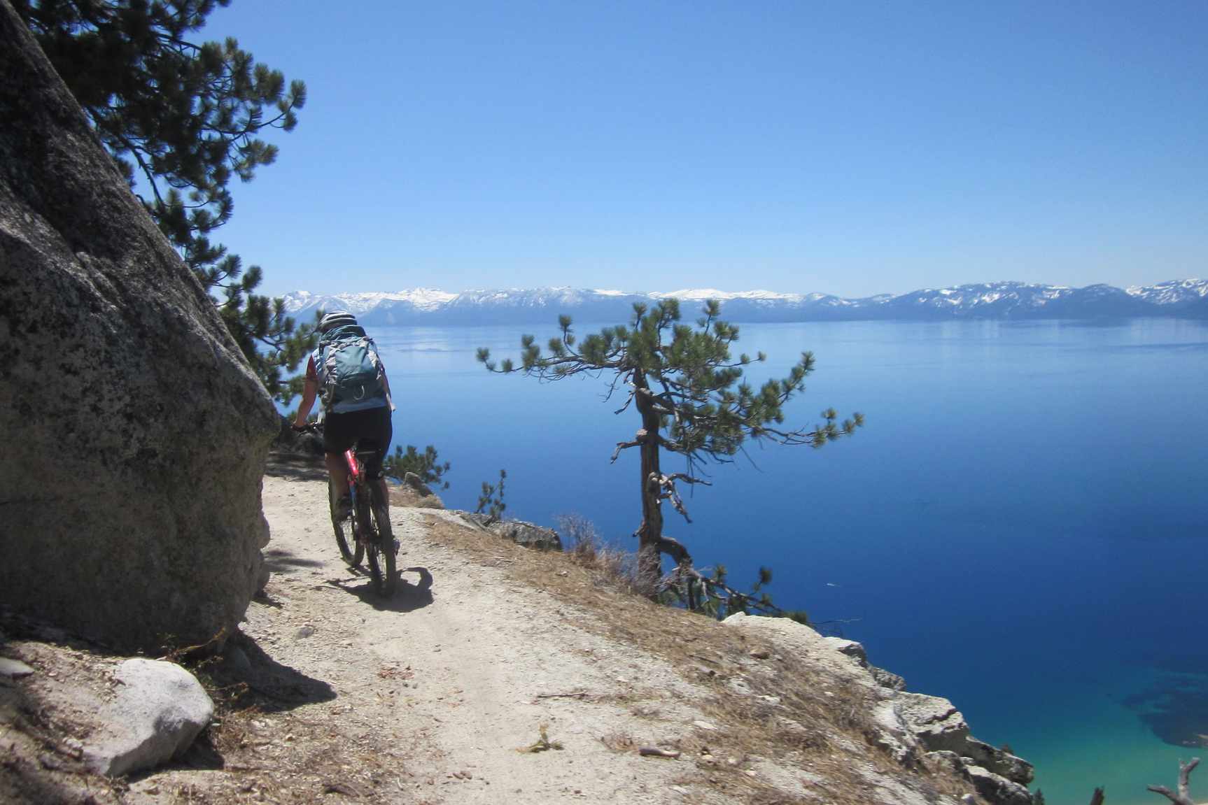 一个骑山地车的人在一条蓝色湖面上的狭窄小道上拐弯。