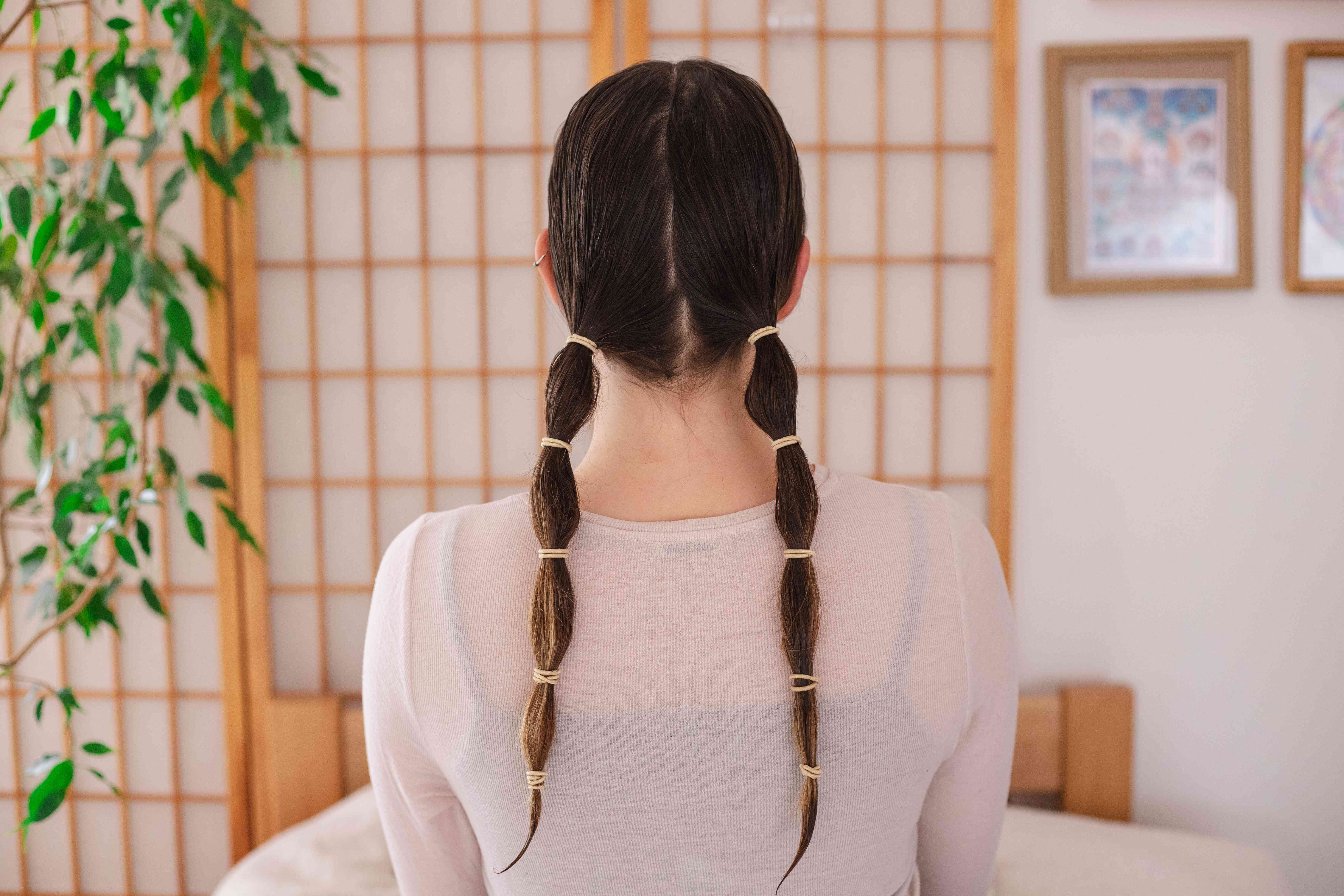 背部拍摄的女性潮湿的头发和两个低马尾辫在多个地方用发带固定