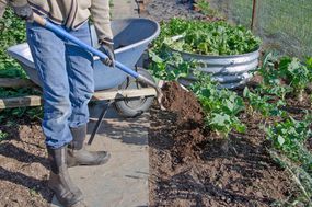 穿靴子的园丁用铁锹给外面的花园加肥料＂width=