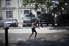 一个女孩穿过水喷泉，在纽约市布鲁克林自治市镇冷却“width=