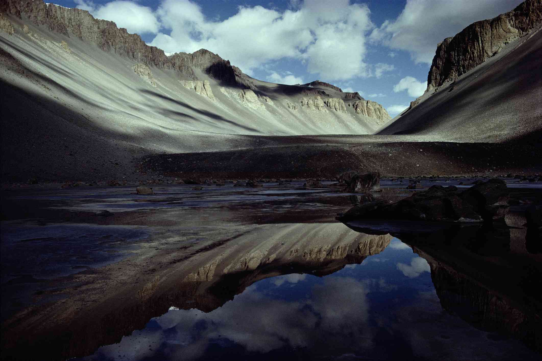 灰色的岩石山脉倒映在一个小池塘的水里