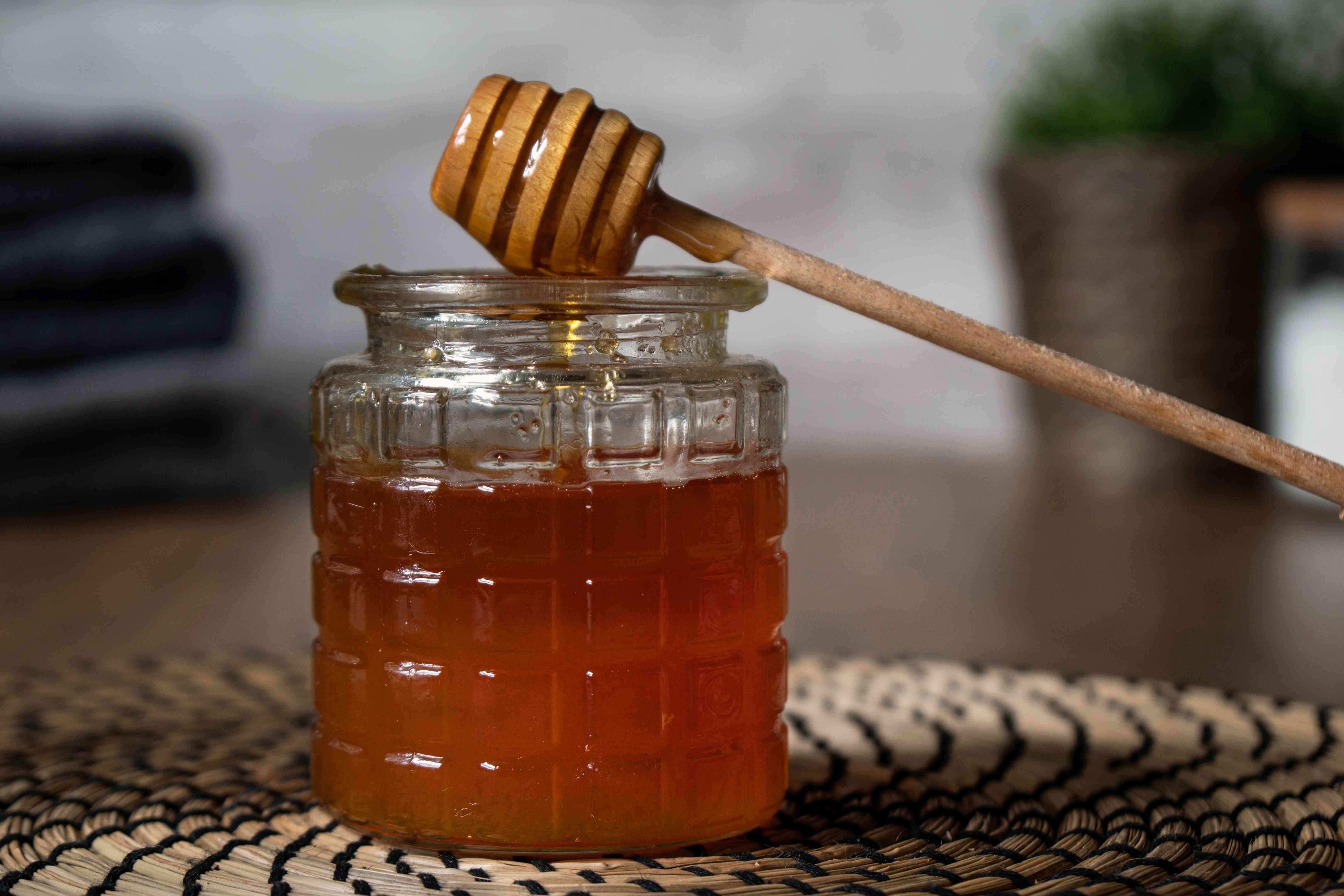 纹理玻璃罐充满蜂蜜与木制蜂蜜勺滴＂width=